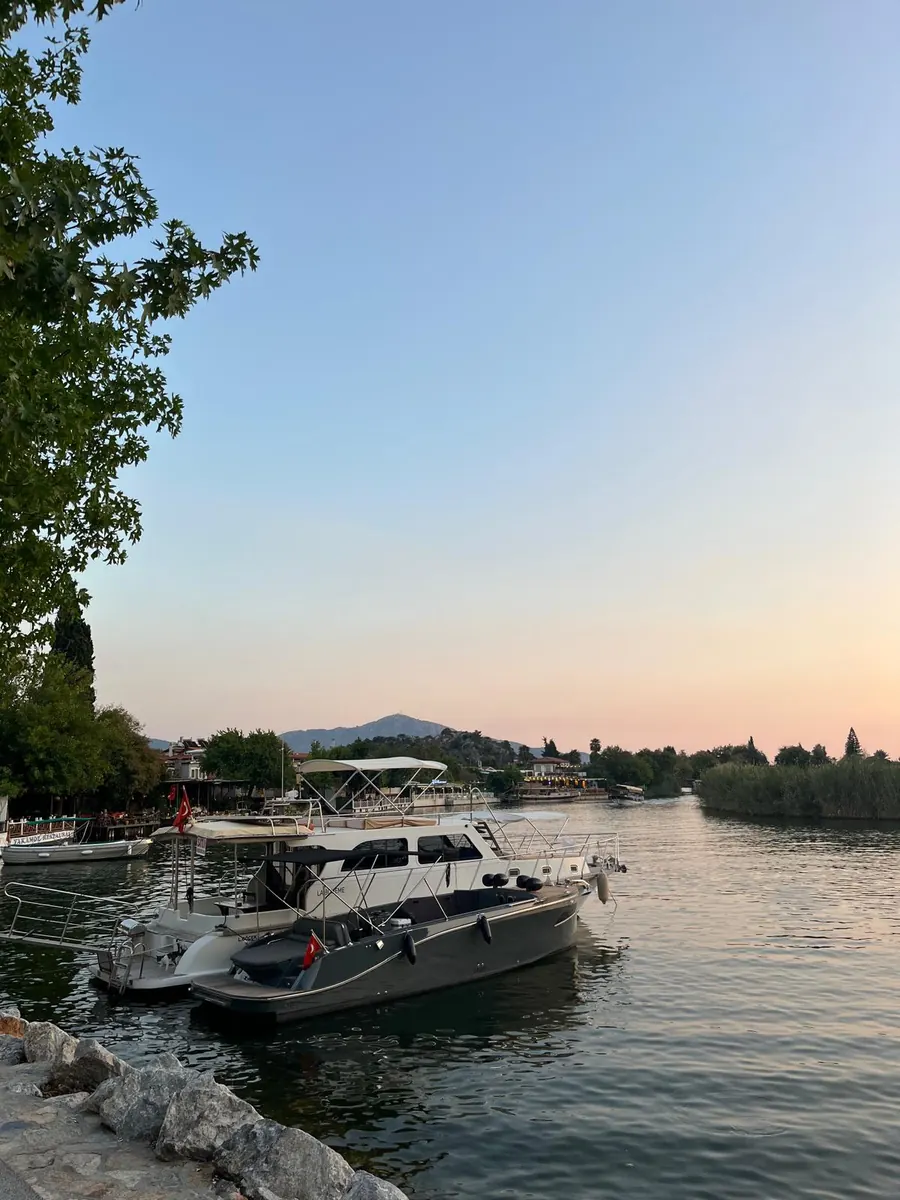 Boats moored on the Dalyan river at dusk, with the riverside restaurants lit on the far bank