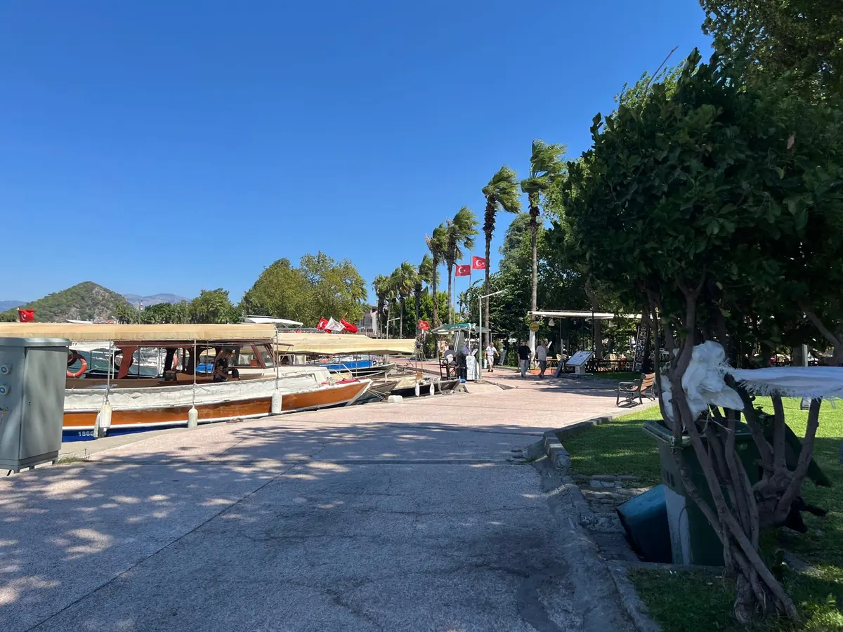 The riverfront promenade in Dalyan with traditional wooden tour boats moored along the quay, palm trees and cafés