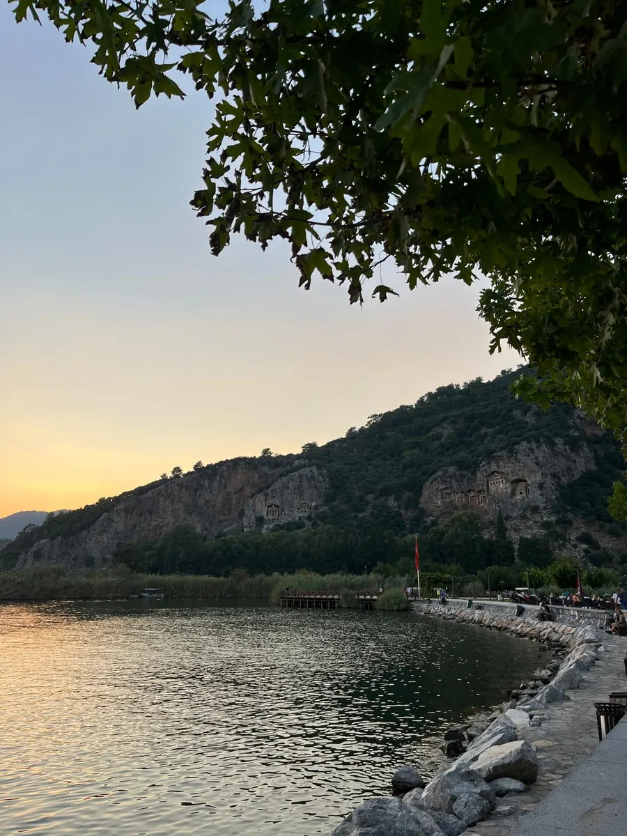 The Kaunos rock tombs at sunset, seen along the Dalyan waterfront with plane tree branches overhead