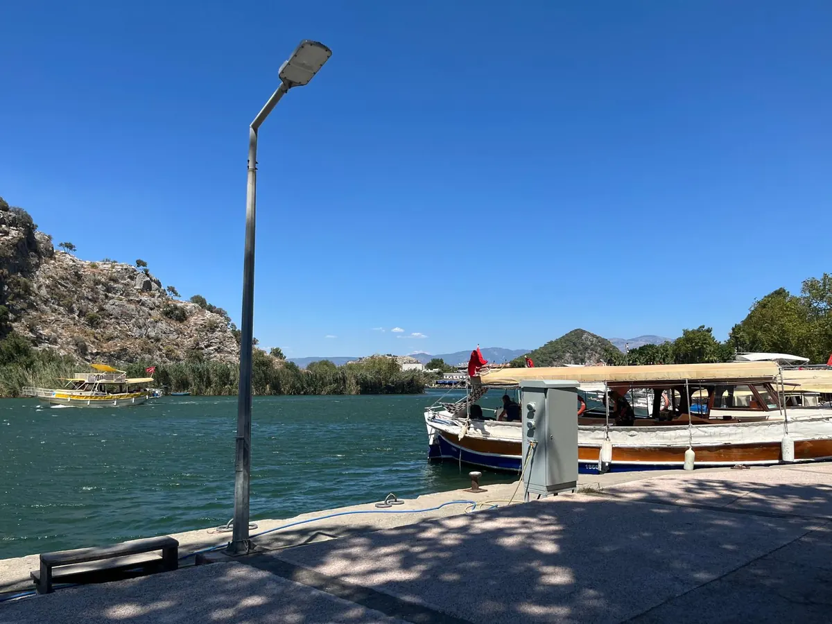 Traditional wooden tour boats moored at the Dalyan quay ready for private charter, with another boat heading up the river